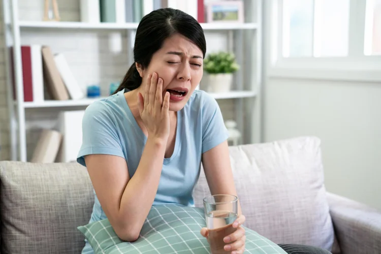 Asian woman feeling pain in her tooth after drinking a glass of cold water.