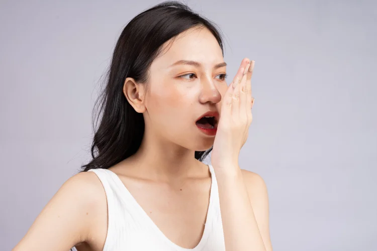 Asian woman checking her breath after a regular dental check-up for teeth scaling and polishing.