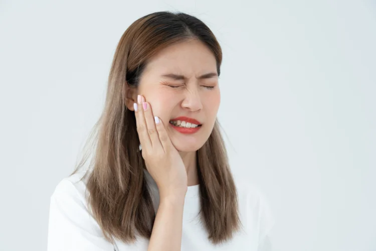 Woman with cheek pain, symptom of a cracked tooth from hard chewing or grinding.
