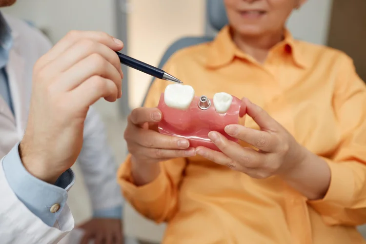 Dentist explaining to patient about dental implant using a tooth model.