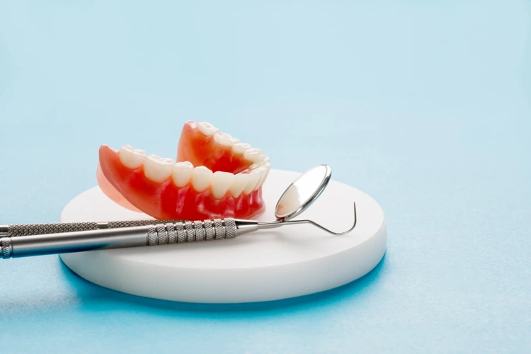 A set of dentures beside dental tools displayed on a white base.