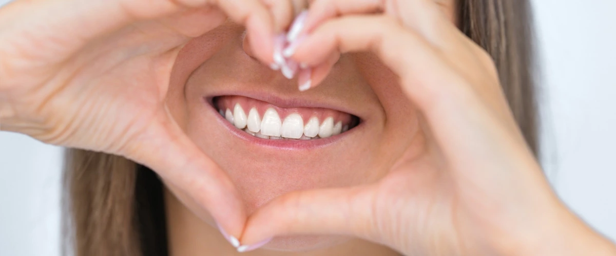 Lady putting her hands and forming a heart shape over her mouth to show her beautiful set of white teeth.