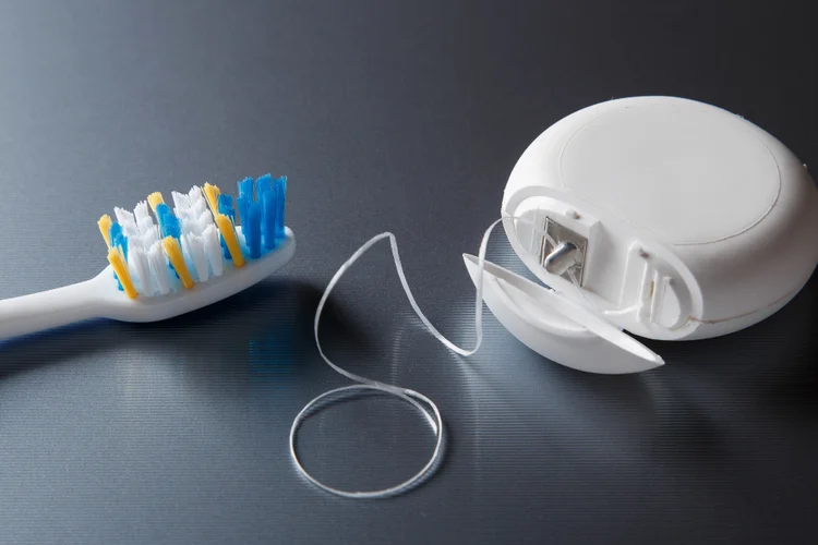 Soft-bristled toothbrush and dental floss on a dark surface, representing essential tools for preventing gum recession through proper oral hygiene.
