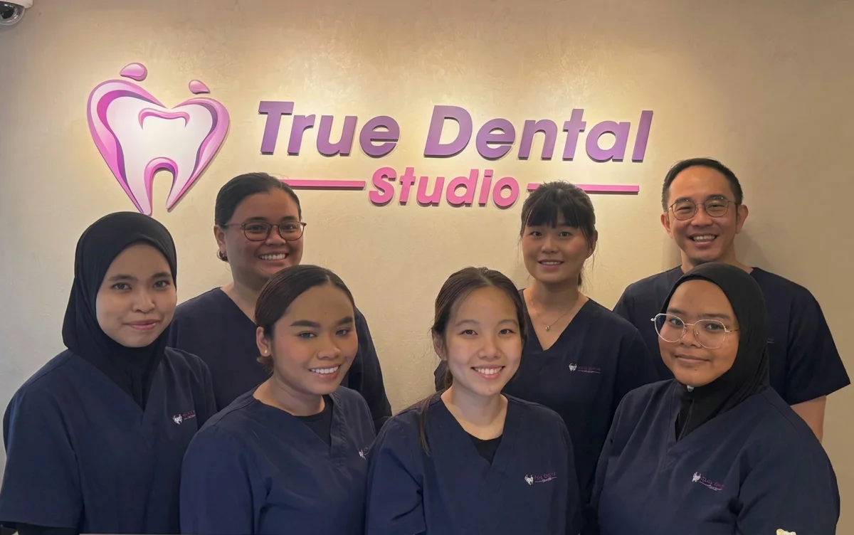 True Dental Studio's dental team smiling in front of the clinic logo at our Ang Mo Kio dental clinic.