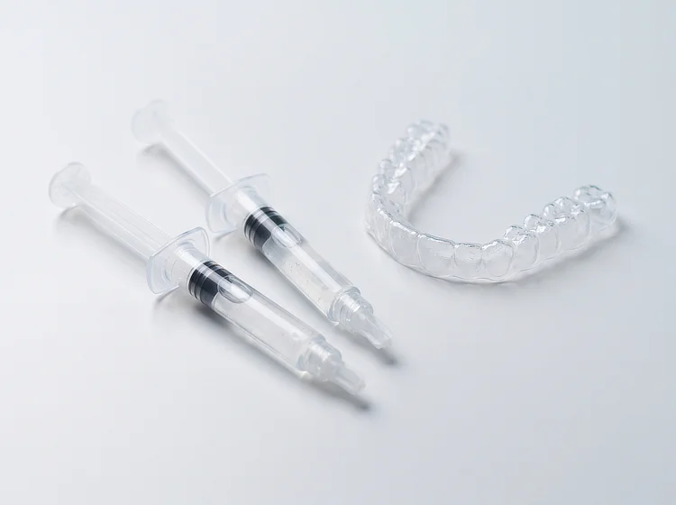 Two syringes of clear whitening gel beside a clear tray on a white surface.