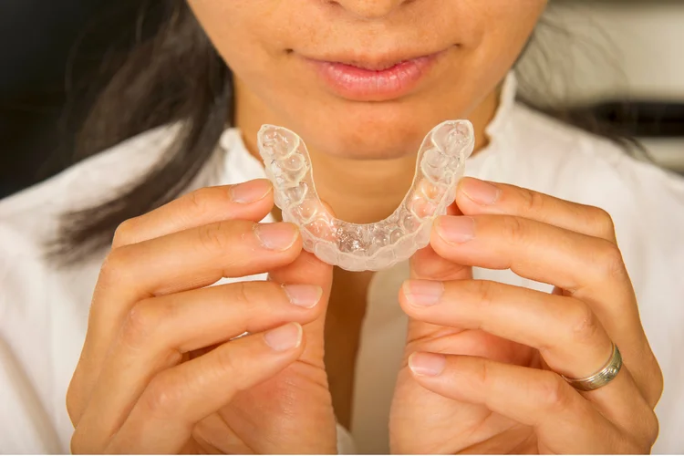 Woman holding teeth whitening trays custom-fitted to her teeth to ensure even whitening gel distribution, protect gums, and reduce sensitivity risk.
