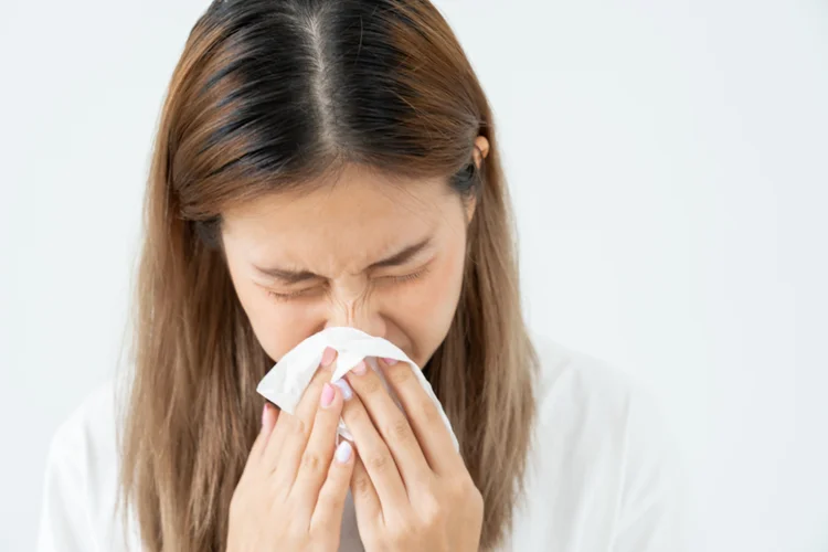 Woman sneezing into a tissue, which should be avoided during sinus lift recovery to prevent graft displacement and pressure on the sinus membrane.