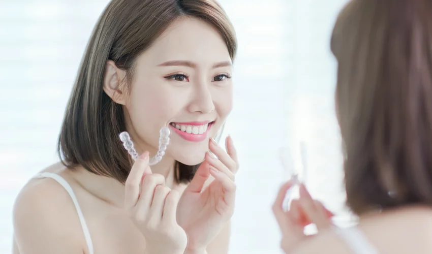 Young Asian lady removing her Invisalign trays to clean and soak them with a specialised cleaner, ensuring effective treatment and maintaining oral health.